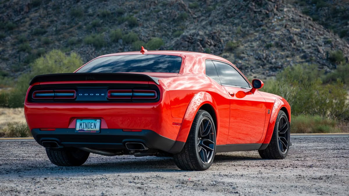 A striking red Dodge muscle car parked on gravel with scenic mountain backdrop.